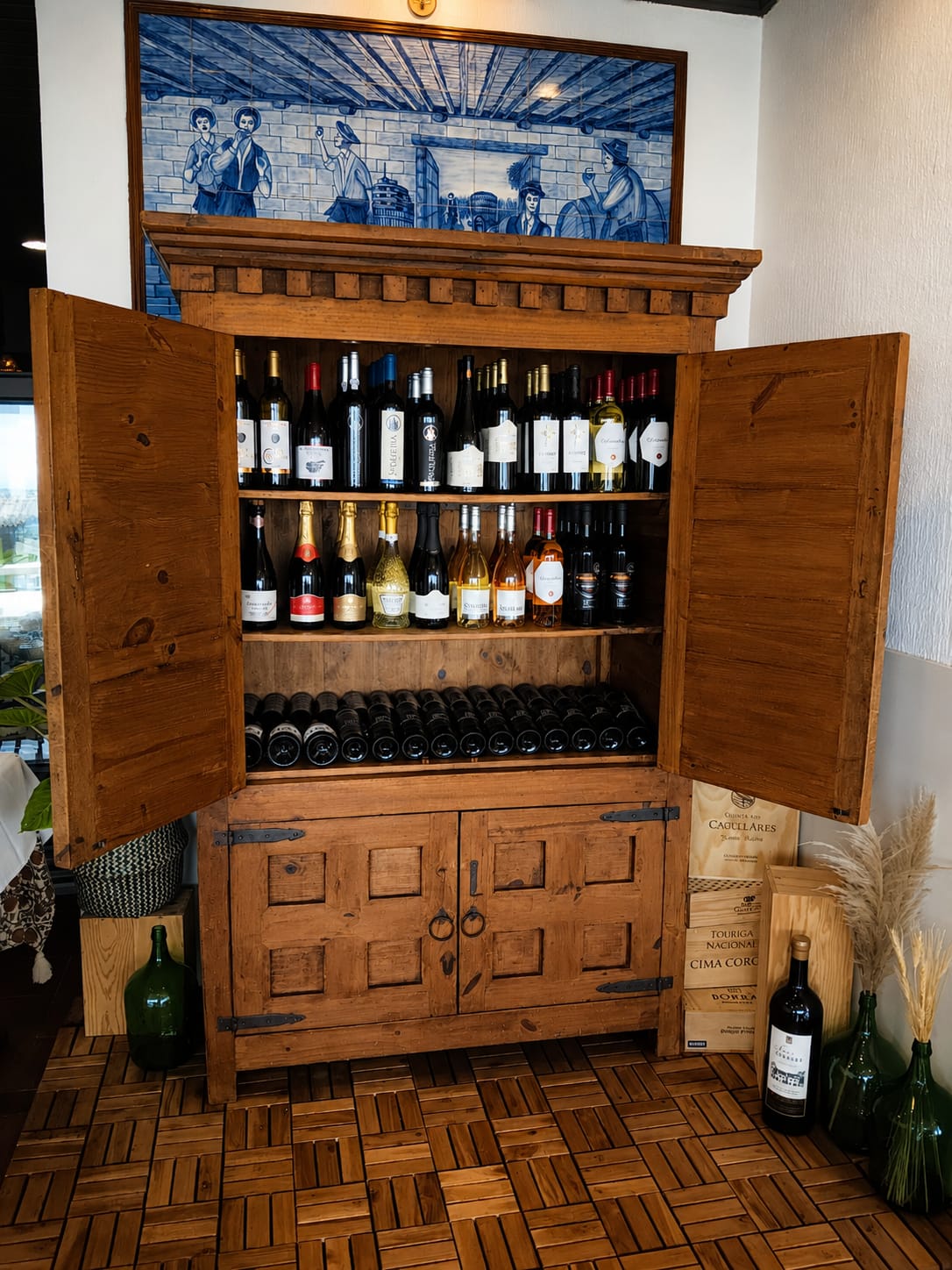 Garrafeira do Terra Mar: móvel rústico em madeira com vinhos verdes, rosés e maduros, sob painel de azulejos portugueses